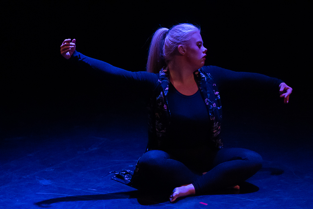 Helen Cherry Helen Cherry, a fair-haired dancer in a black leotard, sits cross-legged onstage, spreading her arms gracefully.
