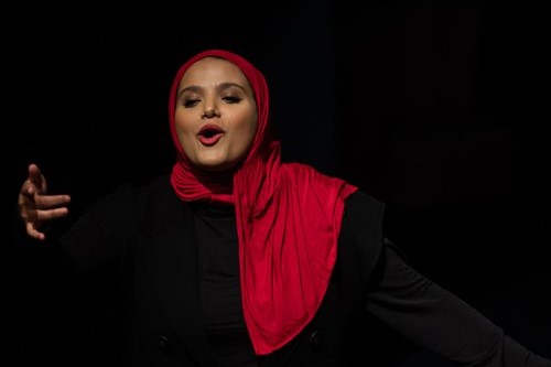 Amina Atiq, a performer wearing a red hijab and black outfit, regales the audience.