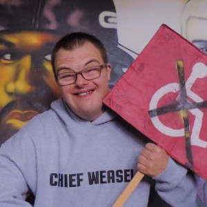 A young man in glasses and a hoodie holds up a placard protesting against cuts to disability services. 