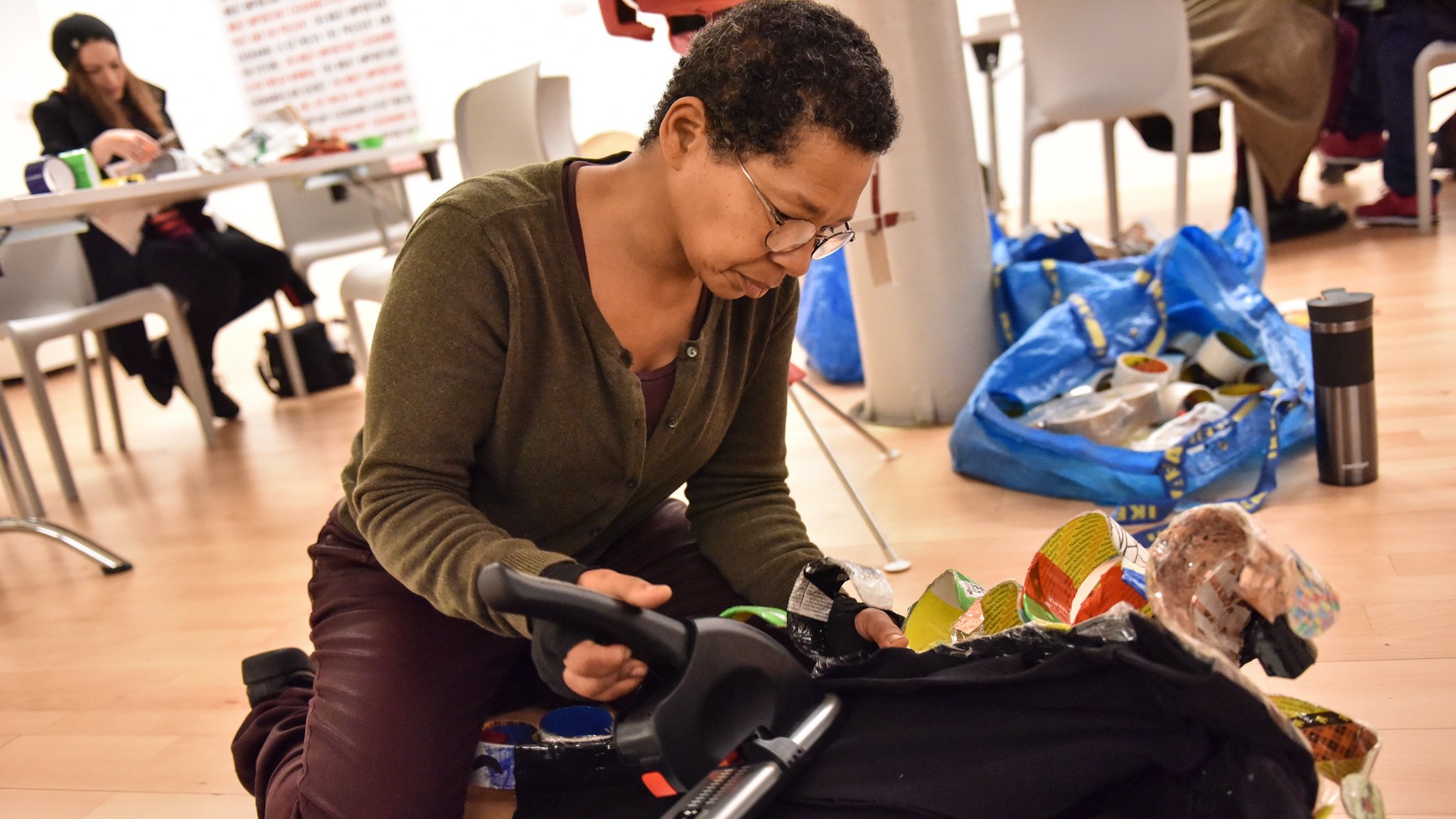 Sculptor, Faith Bebbington, on her knees working on a black piece of fabric with a large stapler.