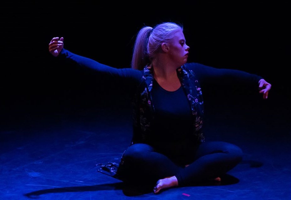 Dancer, Helen Cherry, sat cross-legged on the floor with both her arms outstretched gracefully.