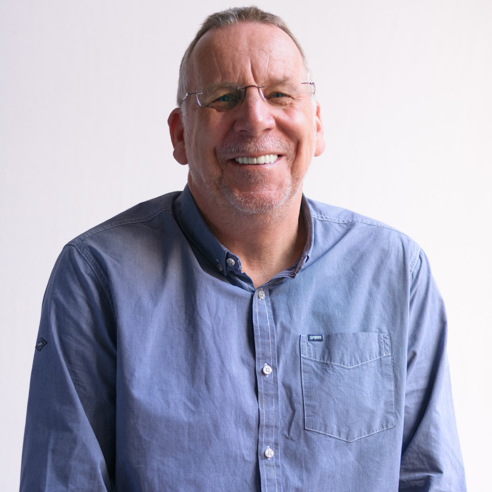 A photo of a man against a white background. He is wearing glasses and a blue shirt