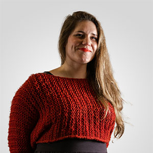 A photo of a young woman with long brown hair, wearing a red sweater and smiling to camera